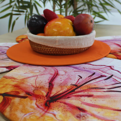 Bajoplato Funda Lirio Acuarela junto a un mantel naranja con un cesto de fruta fresca