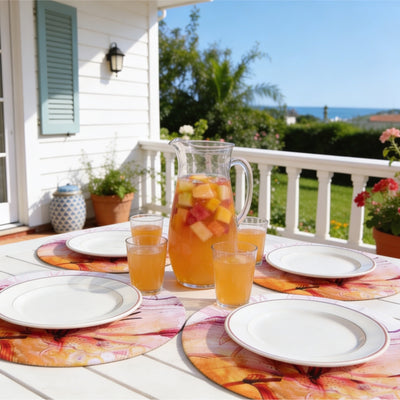 Mesa de terraza con vistas al mar y bajoplatos Funda Lirio Acuarela junto a una jarra de sangría de frutas